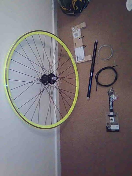 The parts for the rebuild: a new rear wheel with a bright yellow rim, cables, a seatpost and a new stem