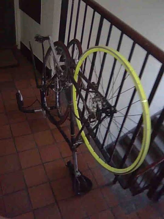 Fixed-gear bike with a yellow rear rim leaning against a stairwell railing